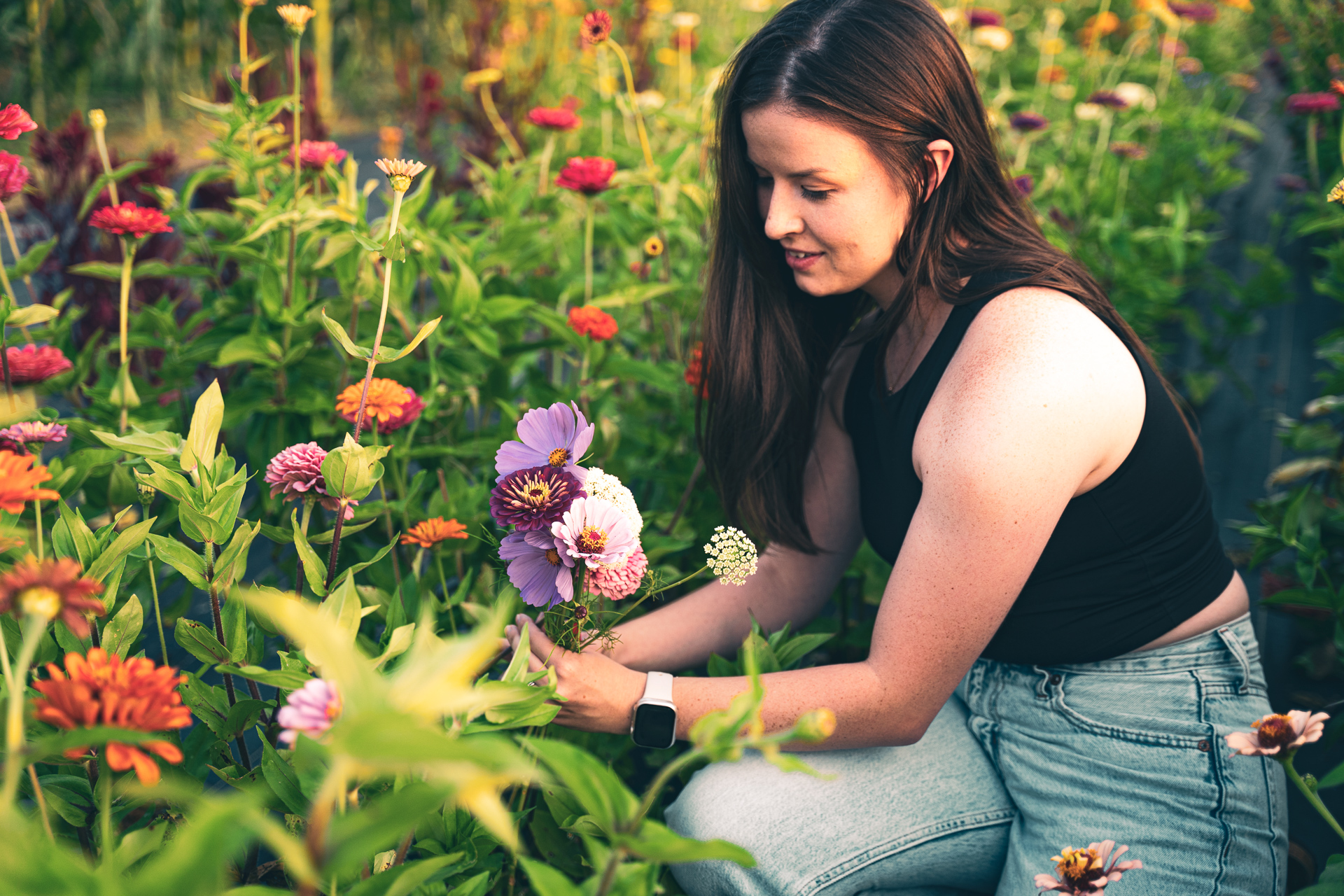A woman kneeling in a row of flowers, arranging a bouquet.